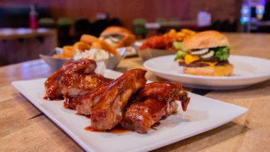 BBQ ribs on a plate with Cheeseburger, wings & onion rings in the background